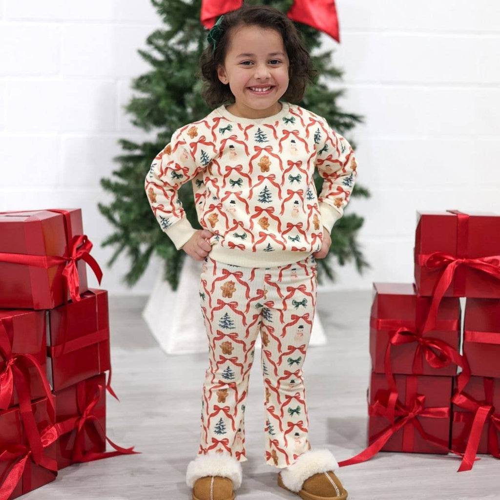 Child wearing a festive pajama set with Christmas-themed design, surrounded by red gift boxes and a decorated tree.