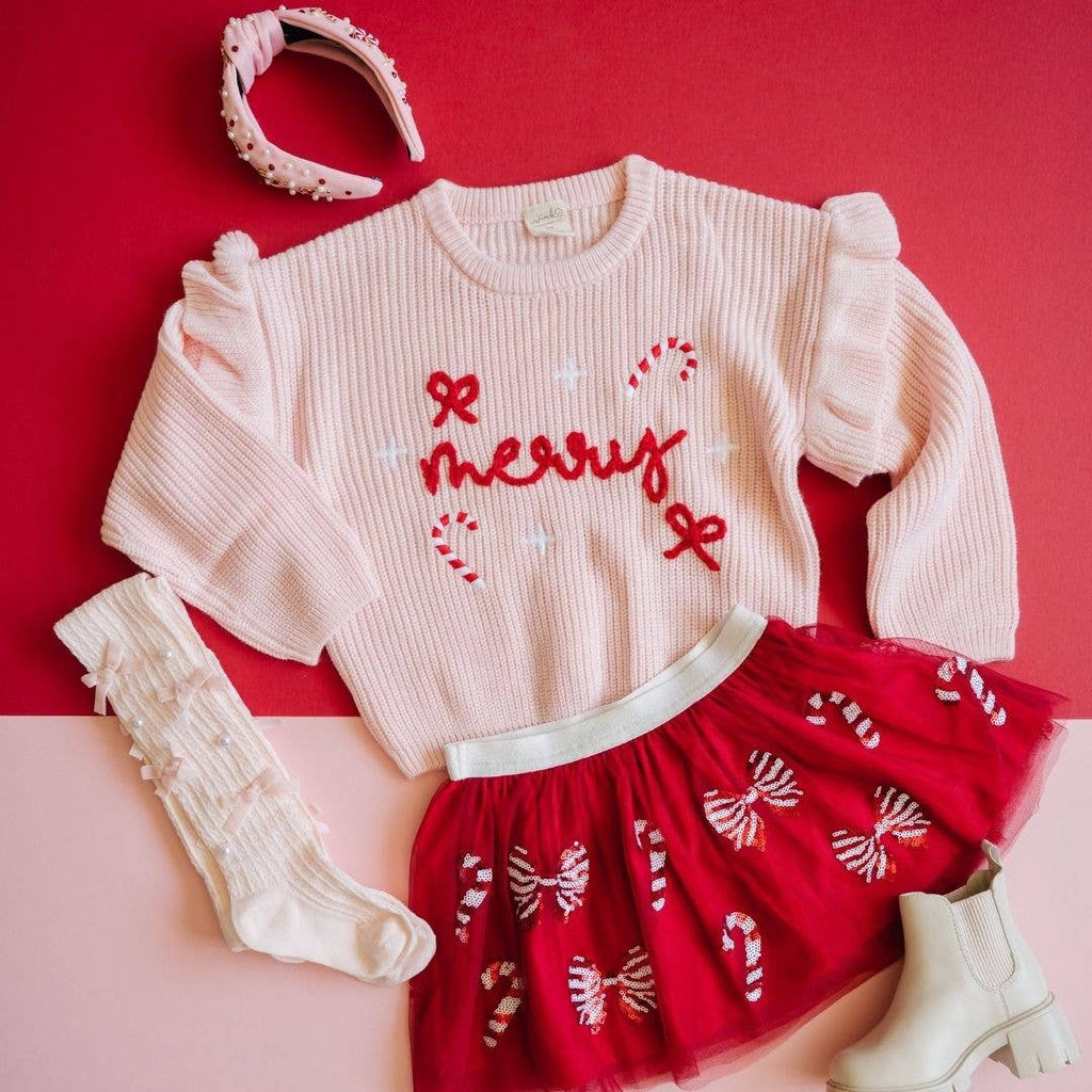 Children's outfit with pink sweater, red skirt, and white boots on a pink background