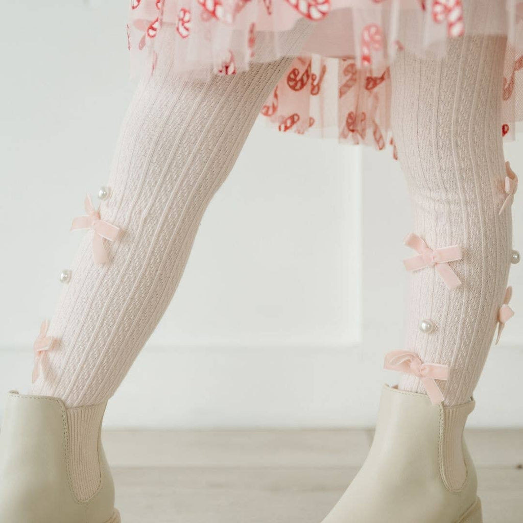 Close-up of legs wearing light pink tights with bow details and a floral dress underneath.