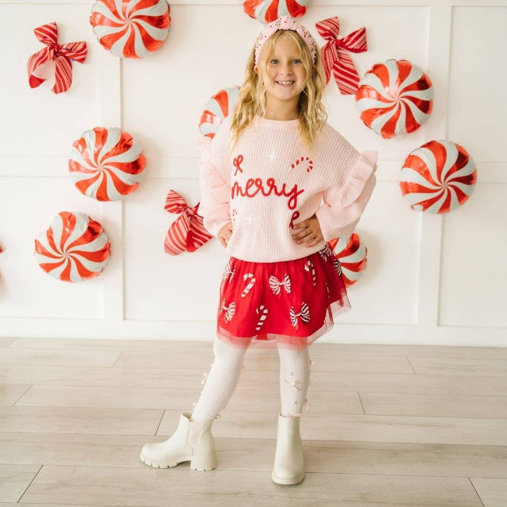 Young girl in festive outfit with candy-themed decorations on a white wall.