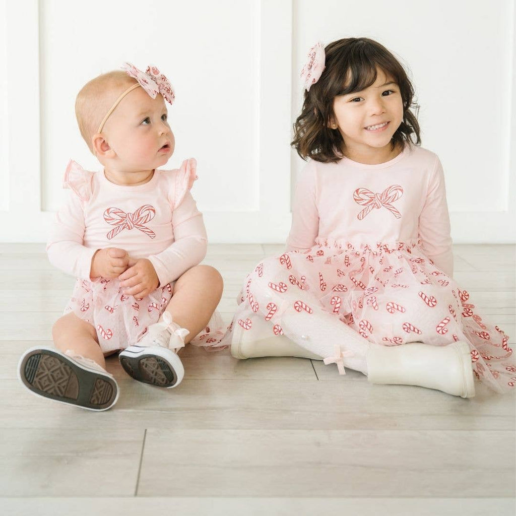 Two young girls in matching pink dresses sitting on a light-colored floor.