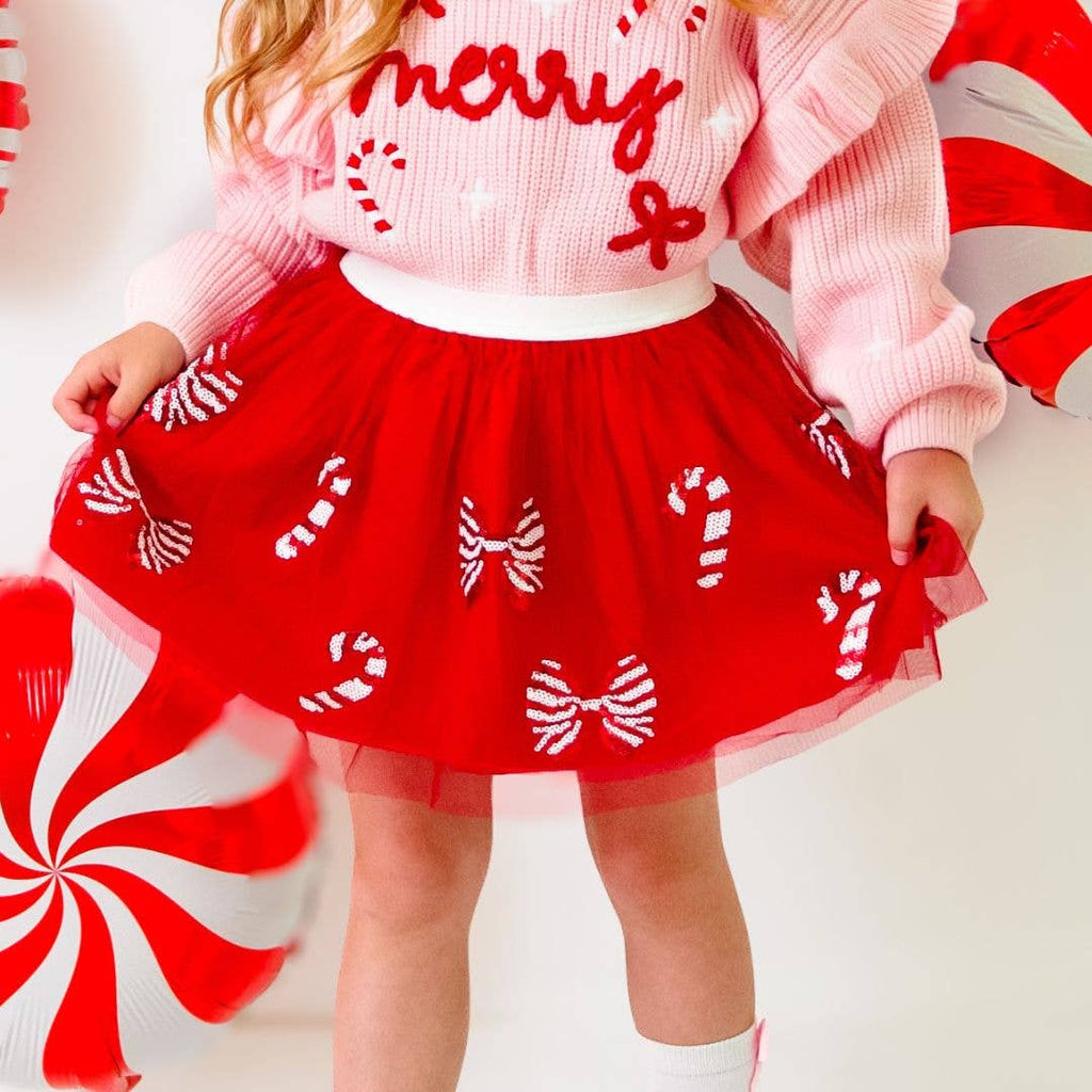 Child wearing a festive outfit with a red skirt and pink sweater on a white background