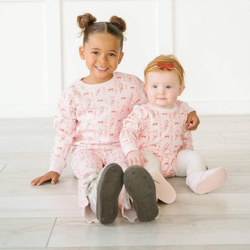 Two children wearing matching pajamas sitting on a white floor.