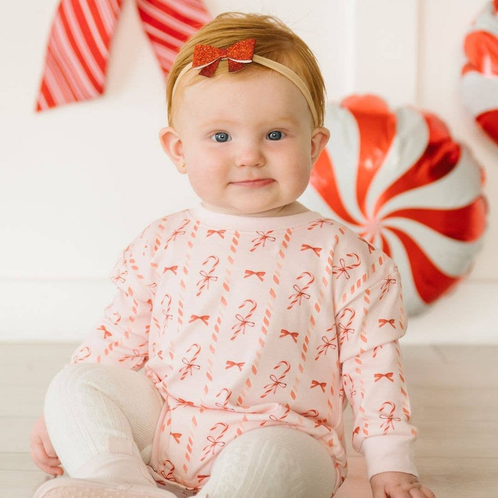 Baby wearing a pink onesie with candy cane pattern in front of candy-themed background