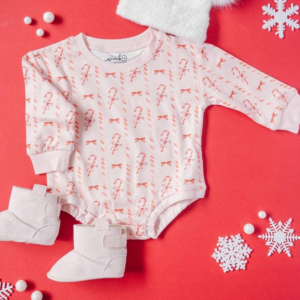 Baby onesie with candy cane pattern, white boots, and snowflake decorations on a red background