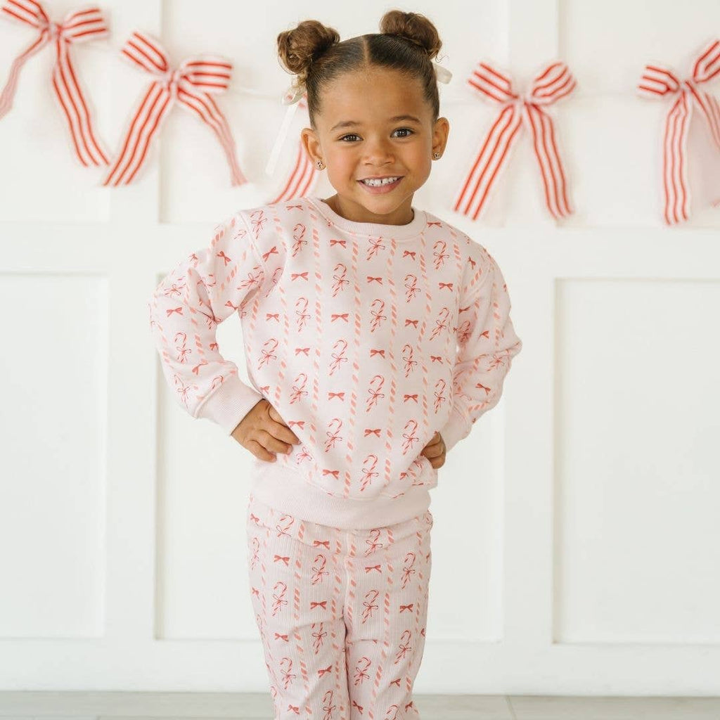 Young girl wearing a pink pajama set with red bows against a white background with red bows.