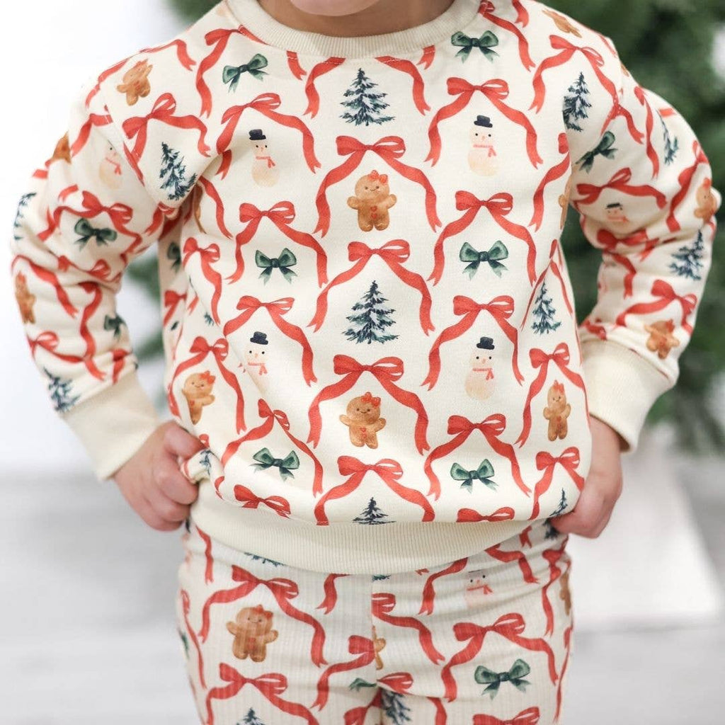 Child wearing a Christmas-themed sweater with red bows, gingerbread men, and trees.