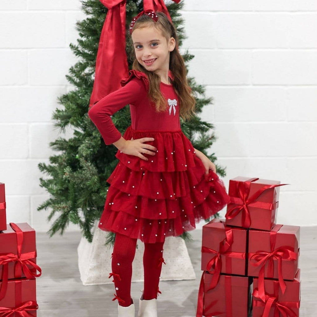 Young girl in a red dress standing in front of a Christmas tree with presents.