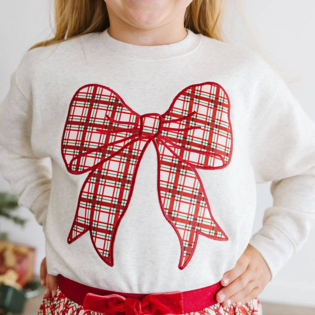 Child wearing a white sweater with a large red plaid bow design.
