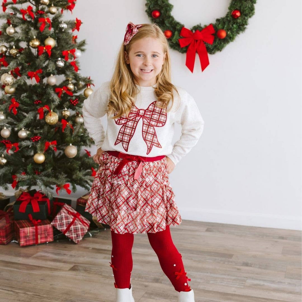 Young girl in festive outfit with Christmas tree and wreath in background