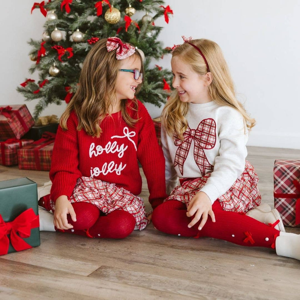 Two children sitting on the floor in front of a Christmas tree with presents.