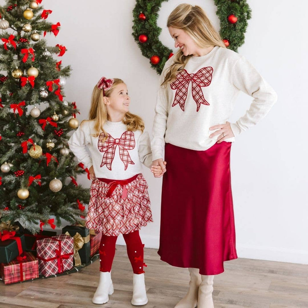 Mother and daughter in matching Christmas-themed outfits standing in front of a decorated Christmas tree.