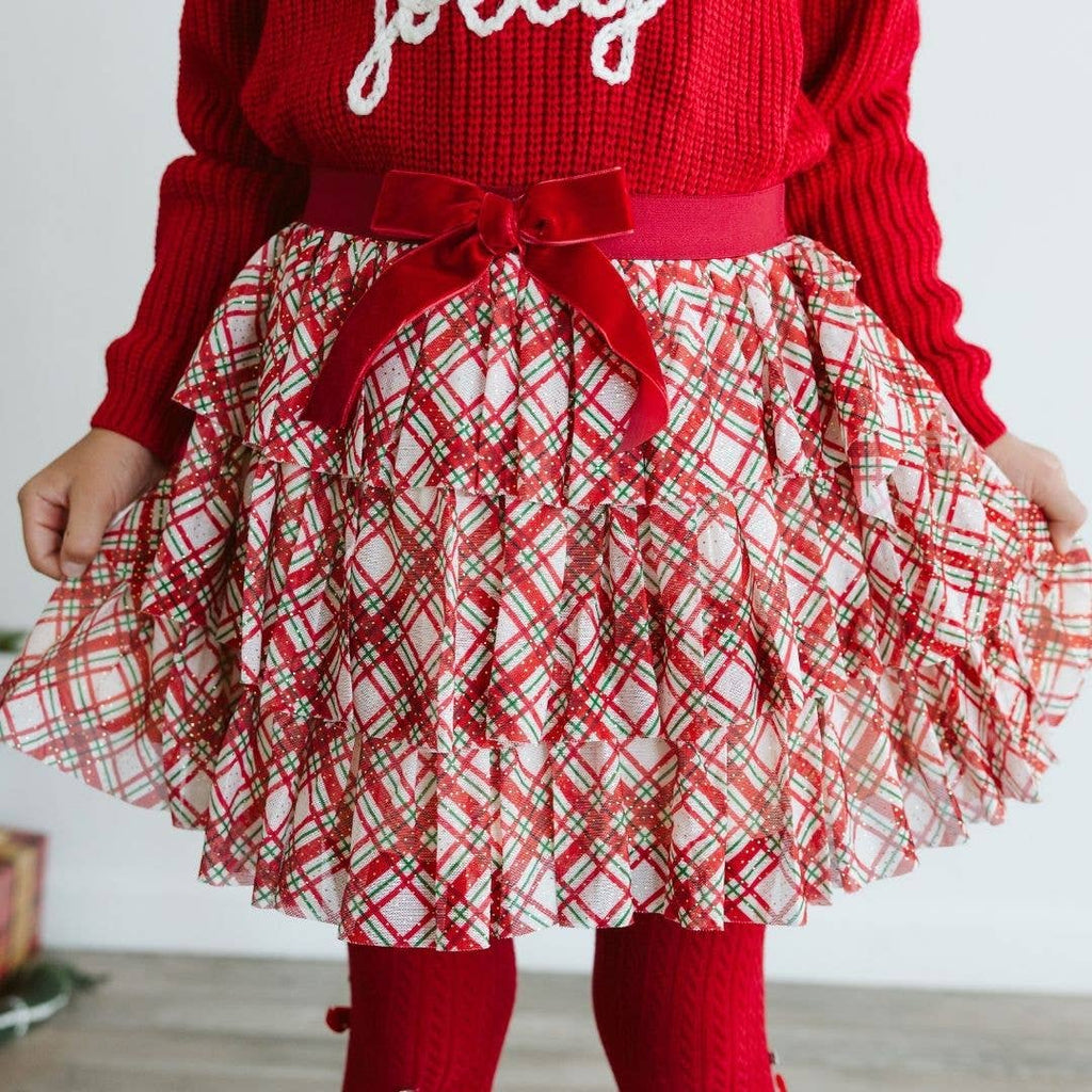 Red sweater with 'jolly' text and plaid skirt worn by a child.