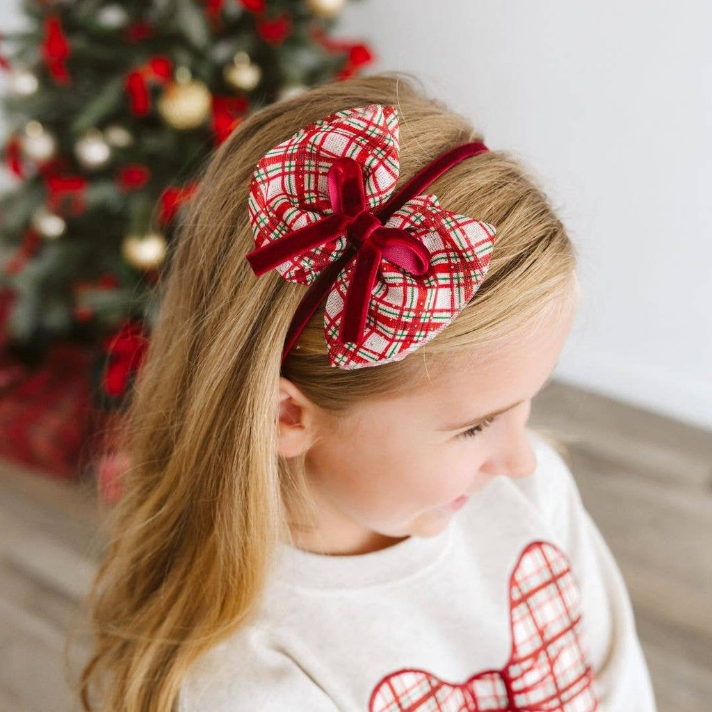 Child wearing a red and white plaid headband with a Christmas tree in the background