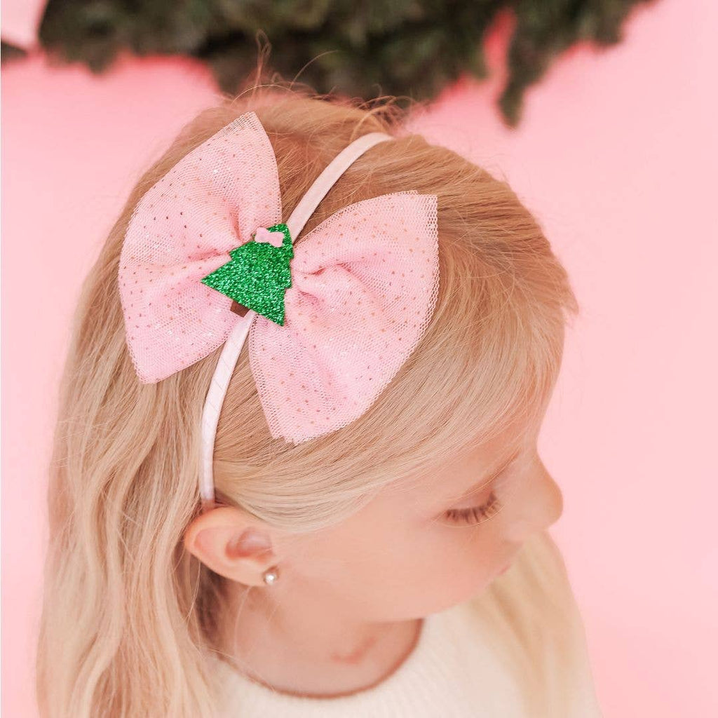 Child wearing a pink bow headband with a green glittery center against a pink background