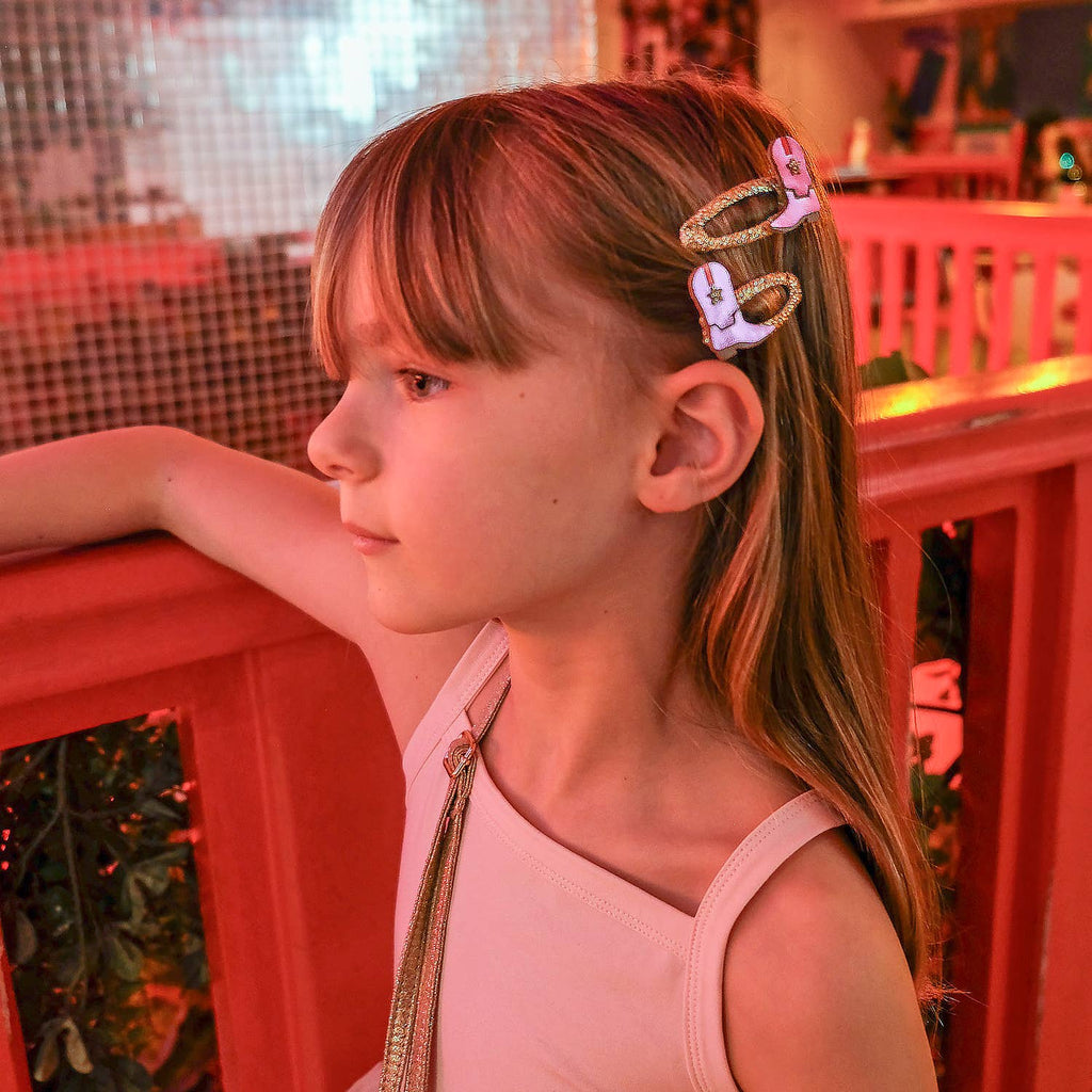 Young girl with a pink hair clip in a pink dress, leaning against a red railing.