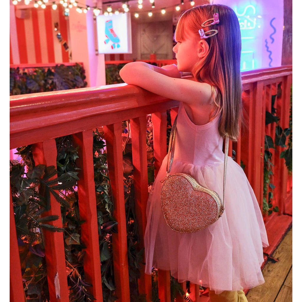 Young girl in a white dress with a glittery heart-shaped bag standing against a colorful background.