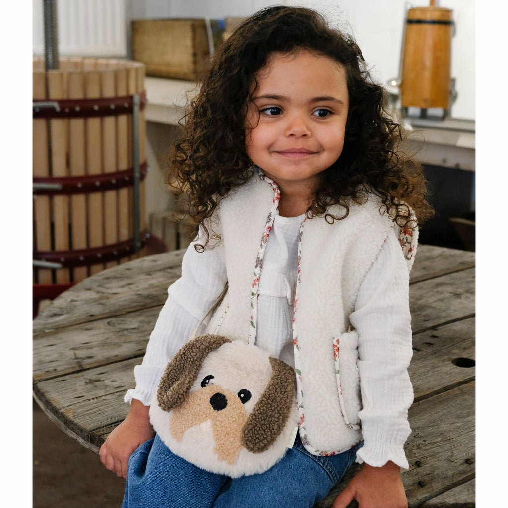 Child holding a plush dog bag on a wooden surface