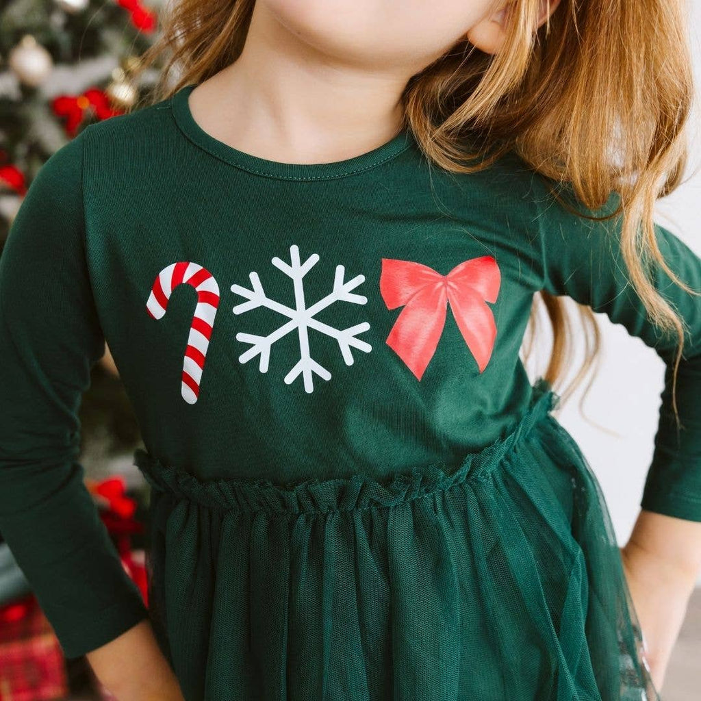 Child wearing a green dress with Christmas-themed graphics in front of a blurred festive background.