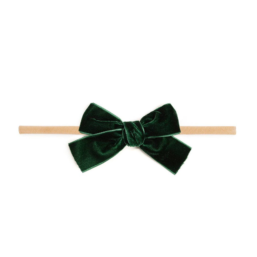 Green velvet bow on a beige headband against a white background