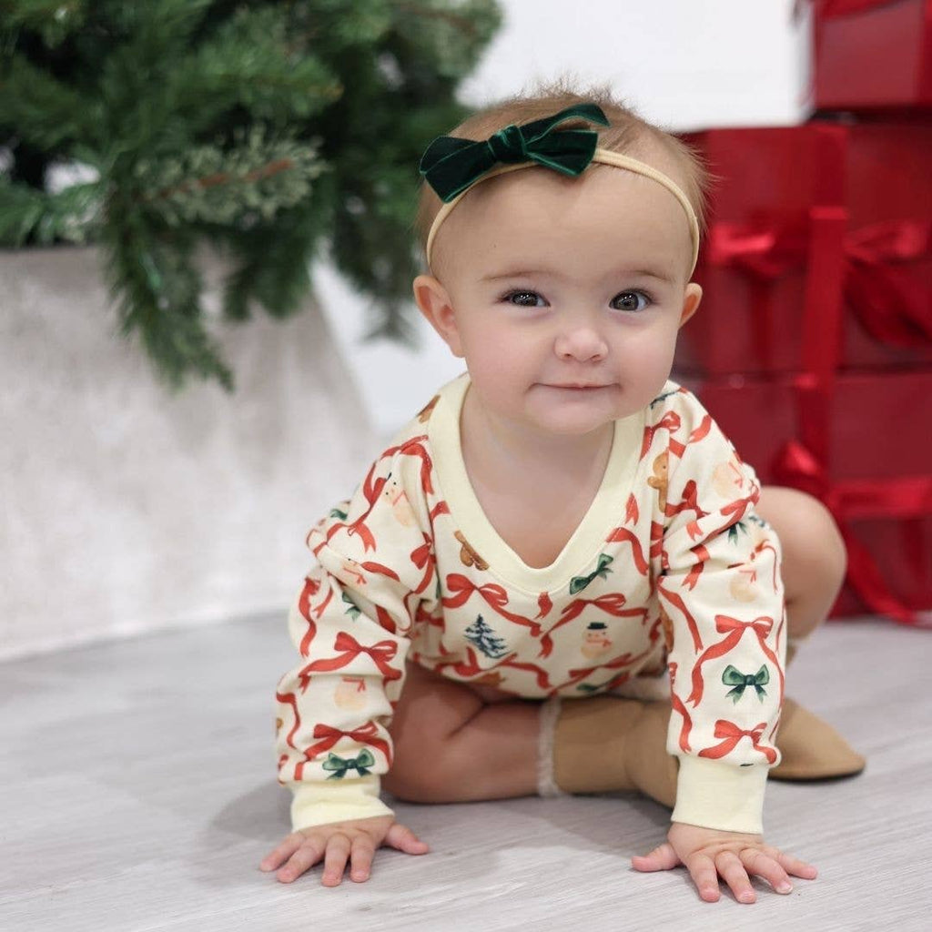 Baby in a patterned onesie with Christmas decorations, sitting on a light surface with a blurred background.