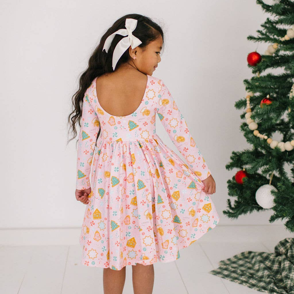Child wearing a floral dress standing in front of a Christmas tree.