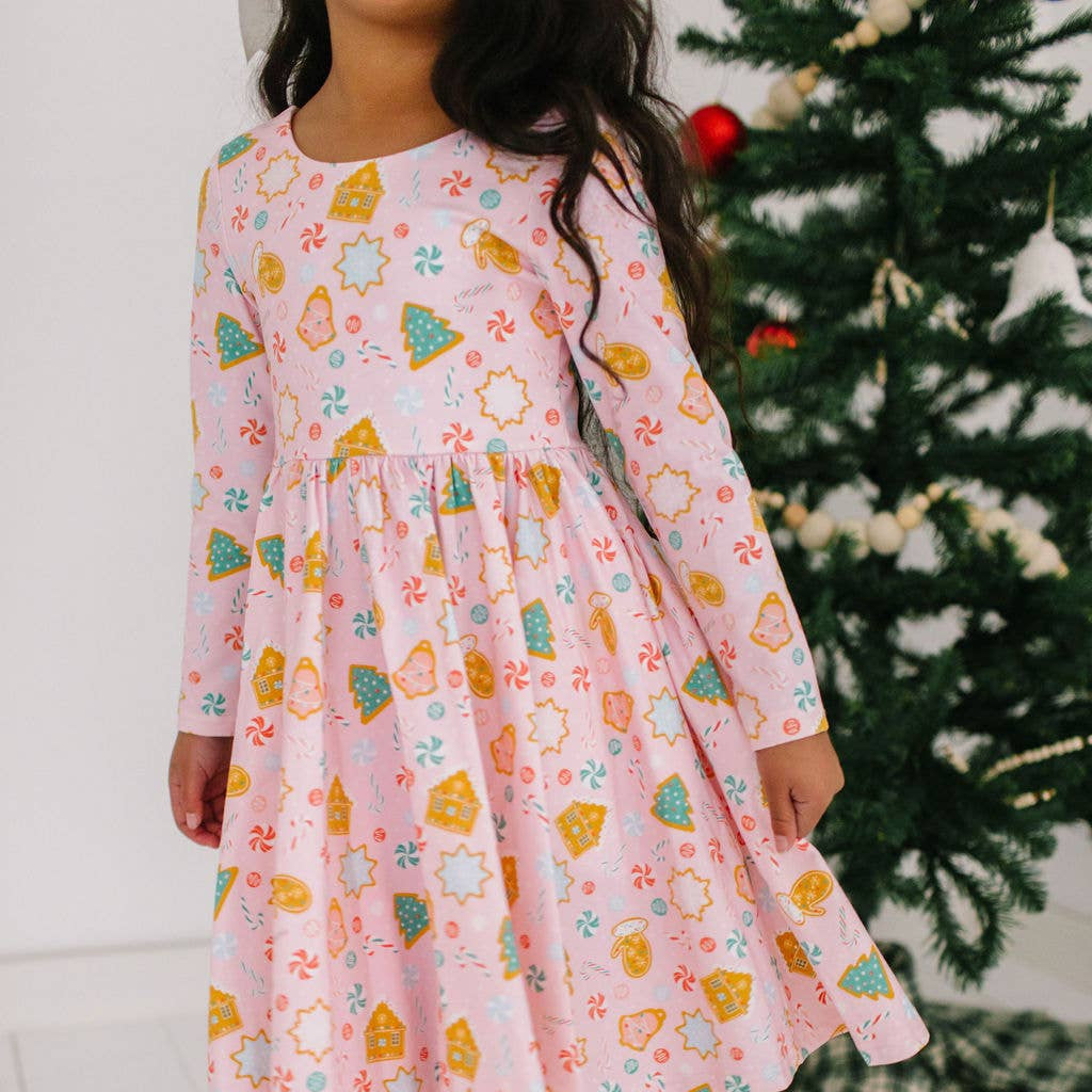 Child wearing a pink dress with colorful patterns in front of a Christmas tree.
