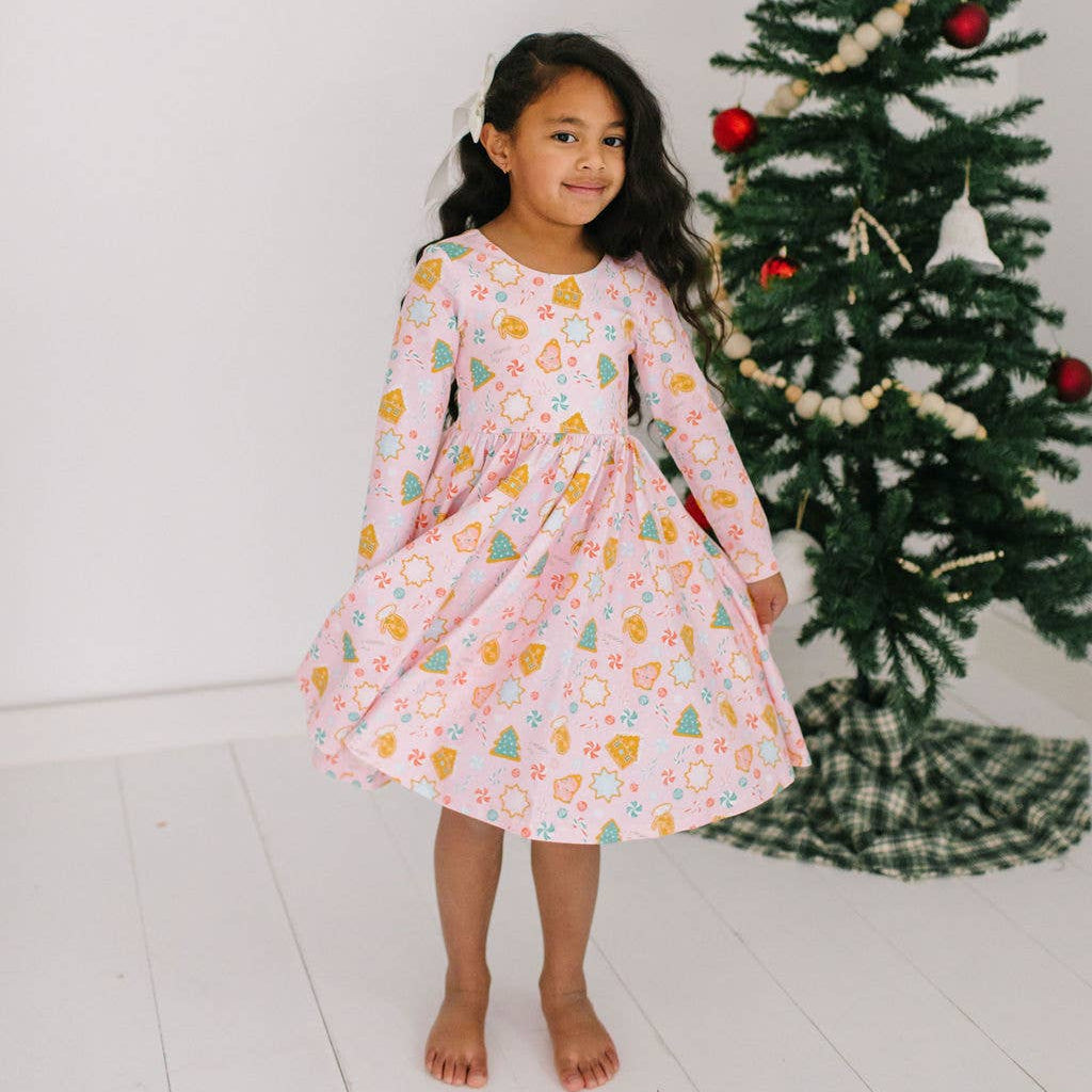 Young girl in a floral dress standing in front of a decorated Christmas tree.
