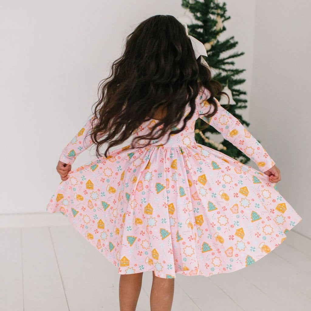 Child wearing a patterned dress standing in front of a Christmas tree.