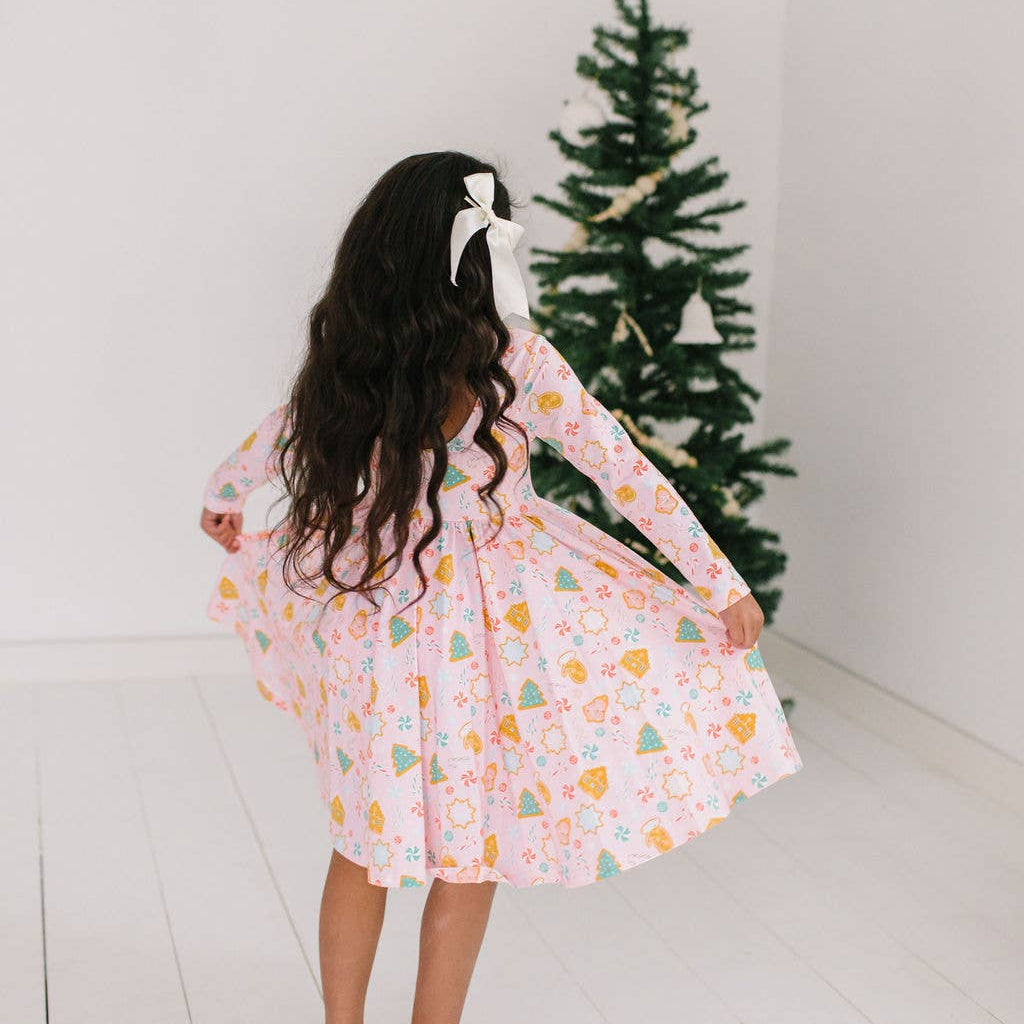 Child wearing a patterned dress standing in front of a Christmas tree.