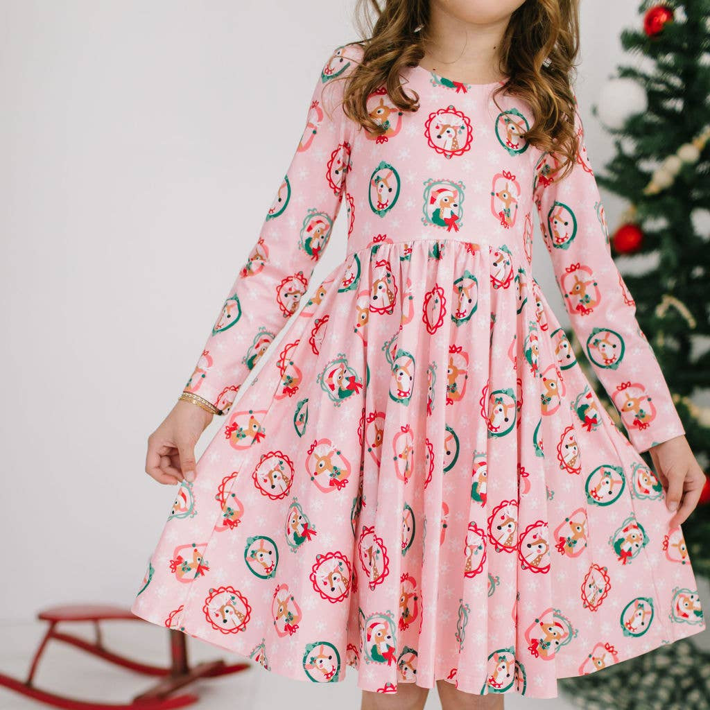 Child wearing a pink dress with a Christmas-themed pattern in a festive setting.