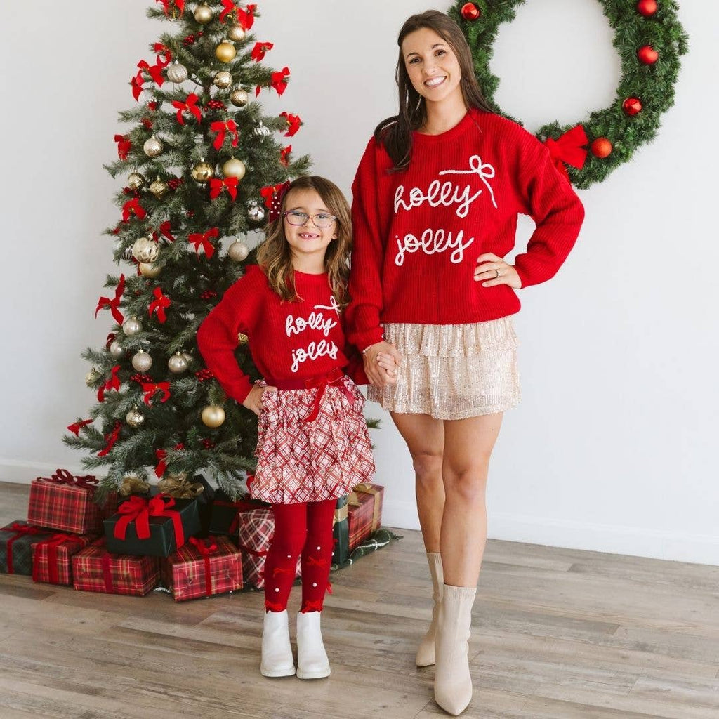 Two people wearing red 'holly jolly' sweaters in front of a Christmas tree.