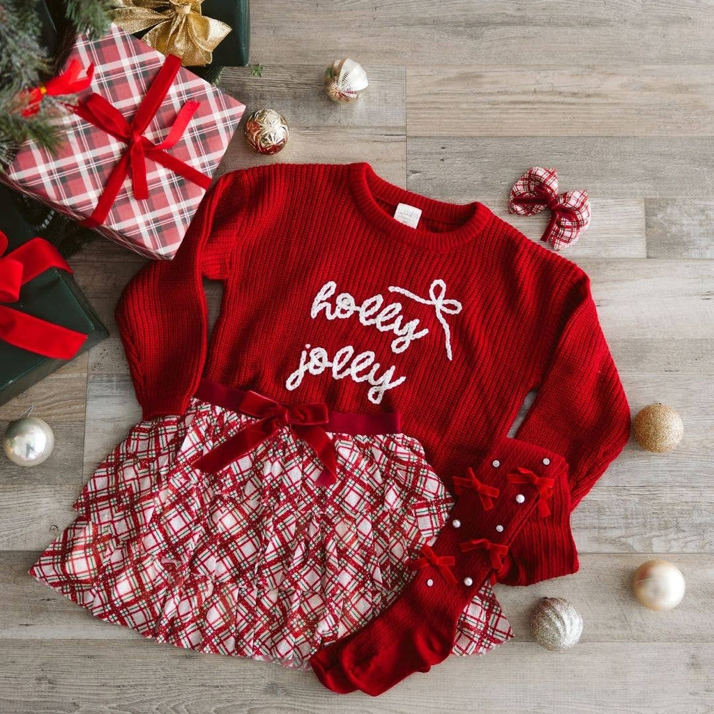 Red dress with 'holly jolly' text on a wooden surface with Christmas decorations.