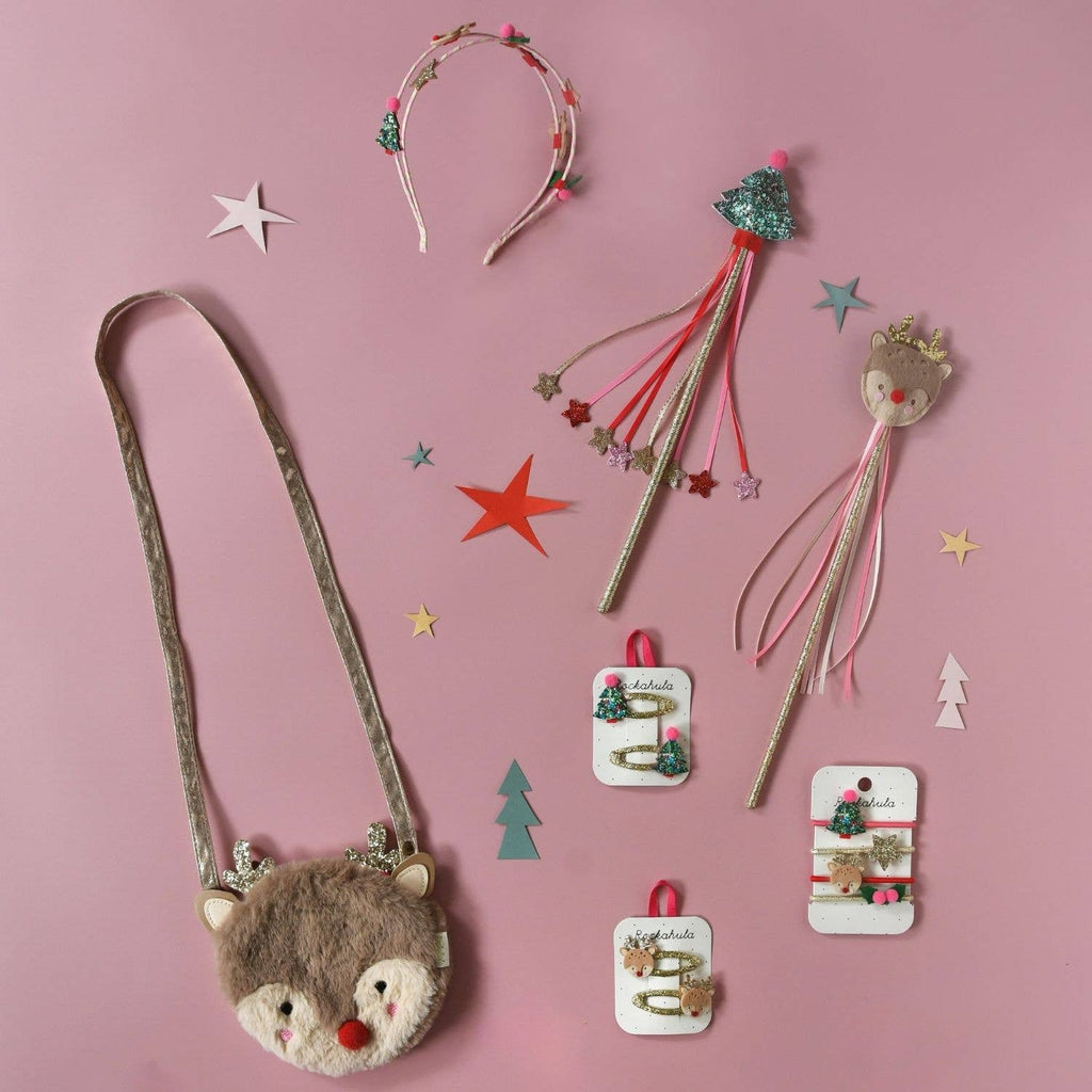 Collection of festive accessories including a reindeer-themed bag, headband, and decorative items on a pink background.