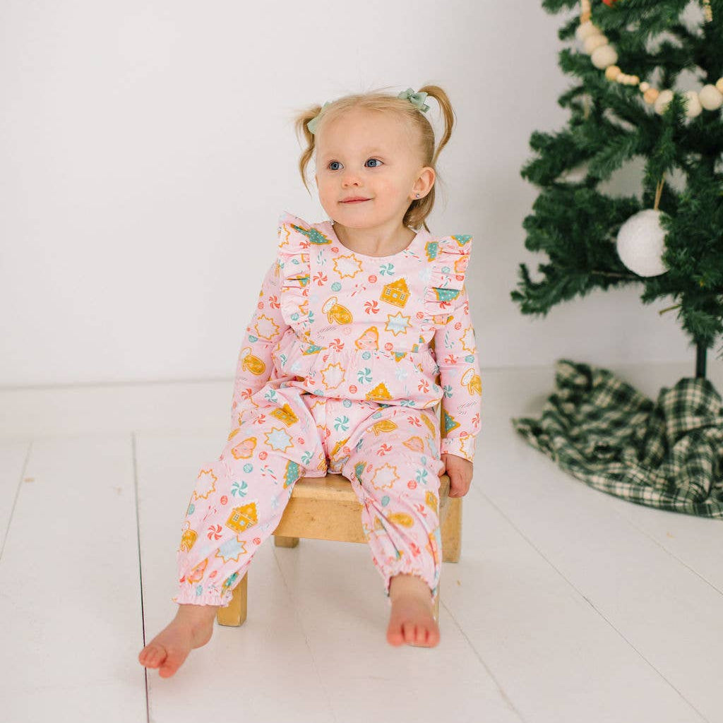 Child in a floral outfit sitting on a stool next to a decorated Christmas tree.