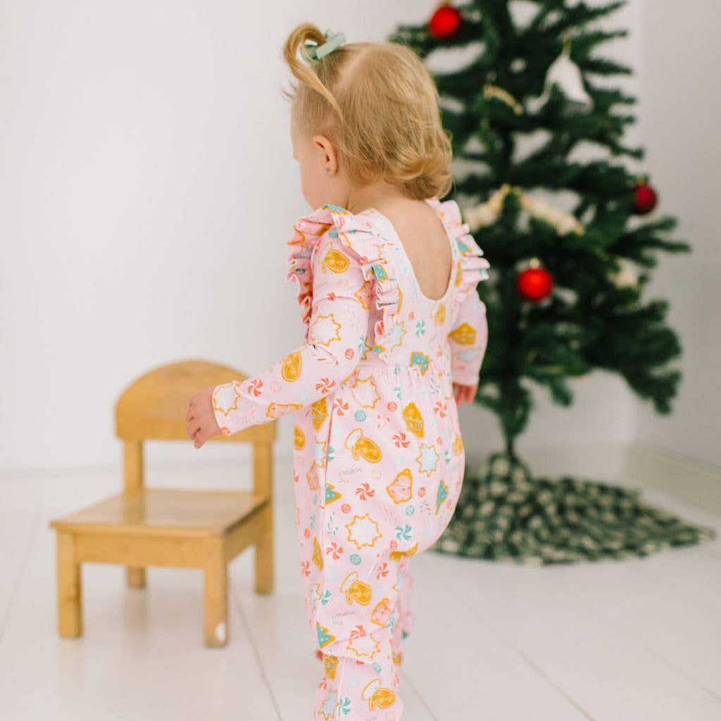 Child in a floral onesie standing near a Christmas tree with ornaments.