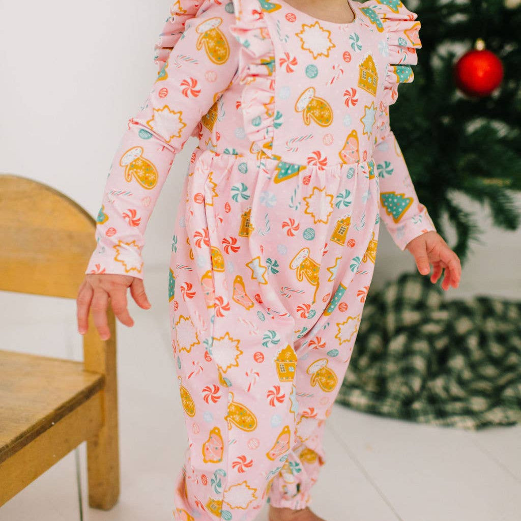 Child wearing a pink floral onesie standing in front of a Christmas tree.