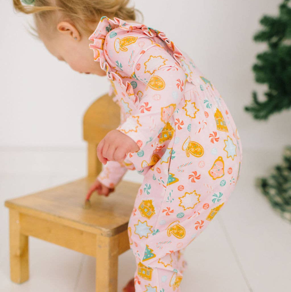 Child in a colorful onesie climbing on a small wooden stool.
