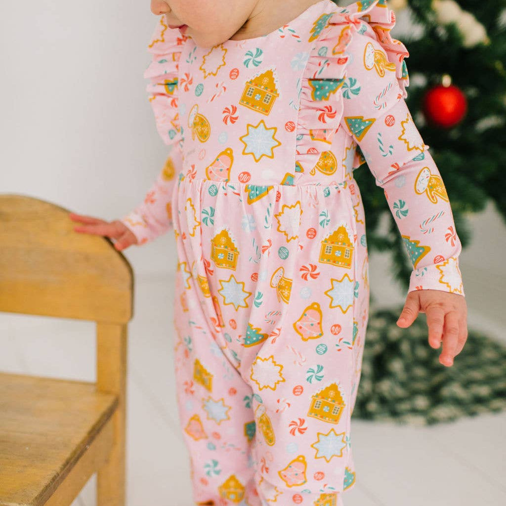 Child wearing a pink pajama set with star and house pattern near a Christmas tree.