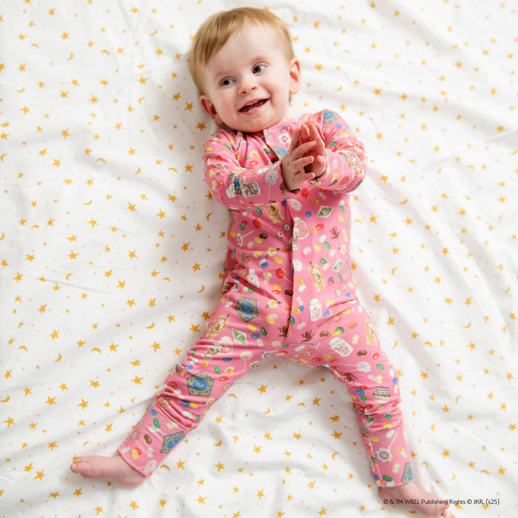 Baby in a pink onesie with cartoon characters on a white blanket with yellow stars