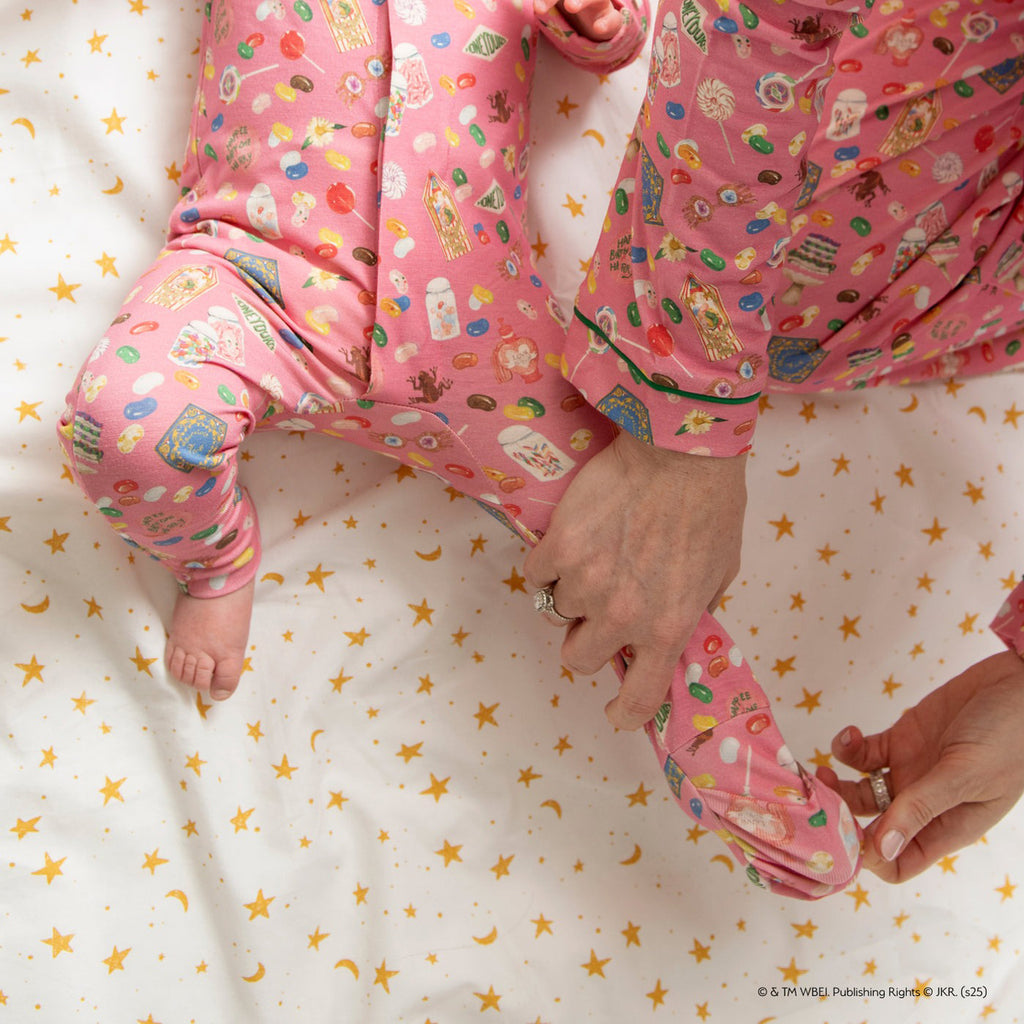 Child in pink pajama pants with cartoon characters on a bed with star-patterned sheets.