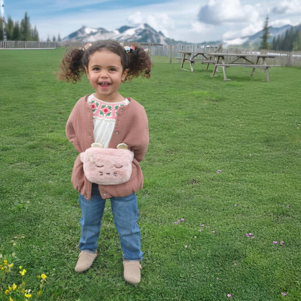 Child holding a pink bag outdoors with mountains in the background