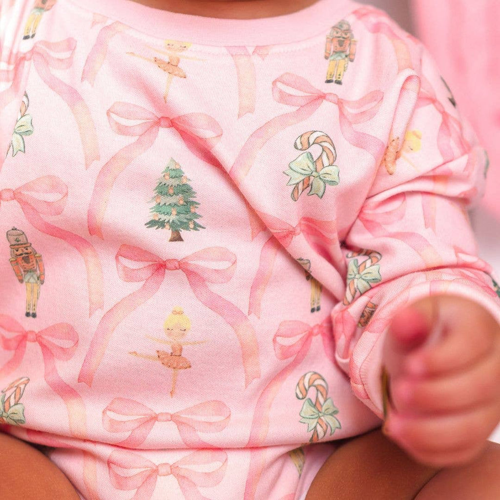 Close-up of a baby's pink outfit with festive patterns including bows, trees, and figures.