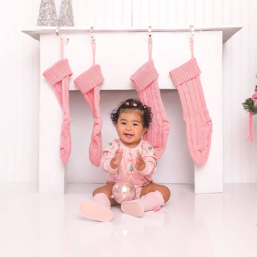 Baby in pink pajamas sitting under pink stockings with a white background
