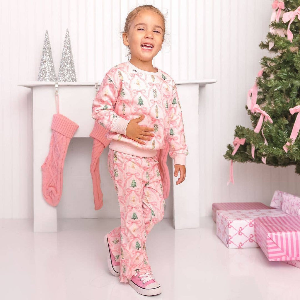 Child wearing pink Christmas-themed pajamas standing in front of a decorated Christmas tree with presents.