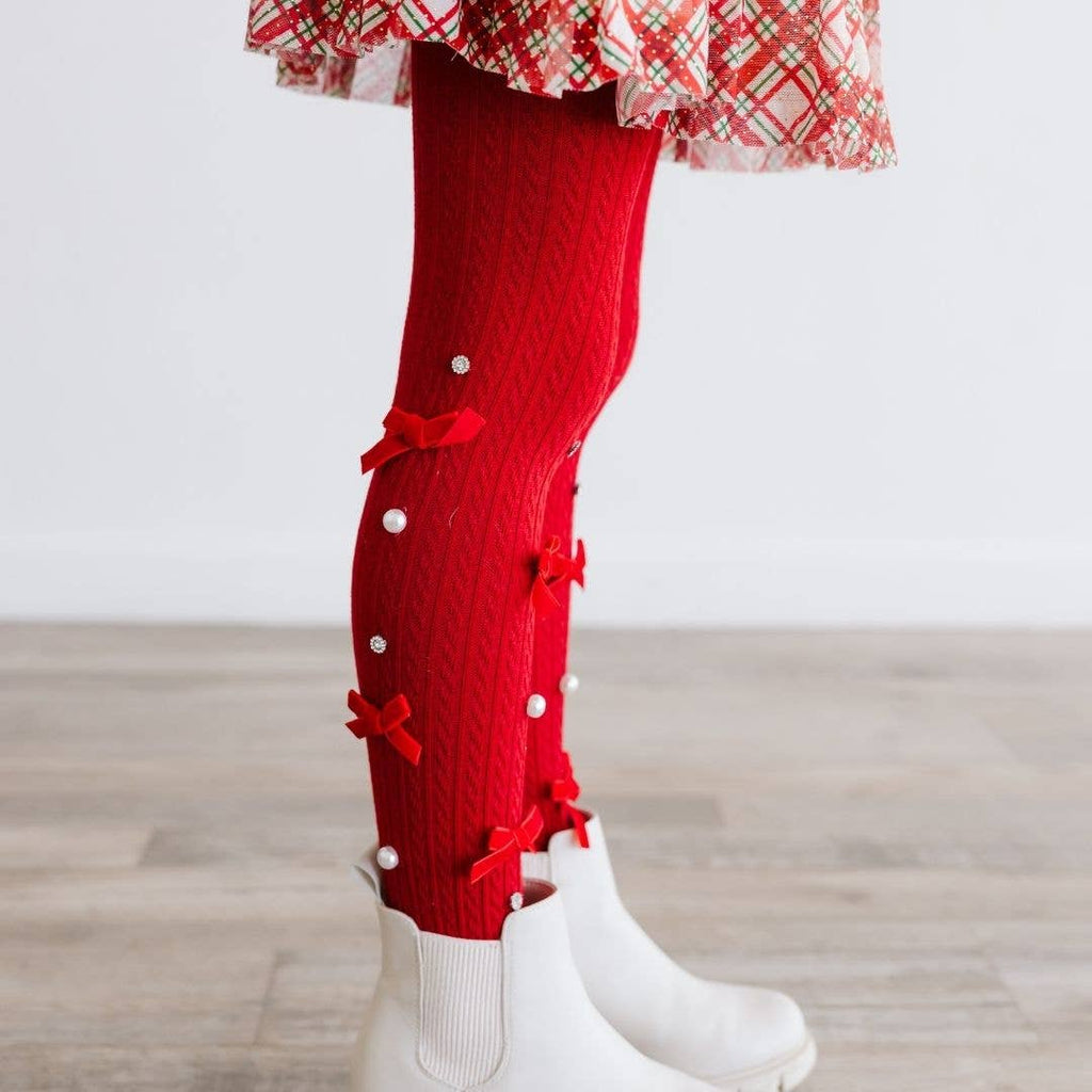 Red tights with decorative bows and white boots on a wooden floor.