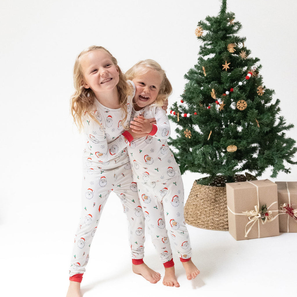 Two children in matching pajamas hugging in front of a decorated Christmas tree with presents.